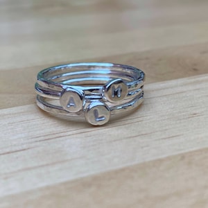 May include: A set of four silver stacking rings with the letters A, L, and M engraved on them.