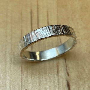 May include: A silver band ring with a textured, wood-like finish.