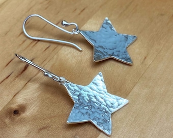 May include: A pair of silver star-shaped earrings with a hammered texture. The earrings have a simple hook closure.