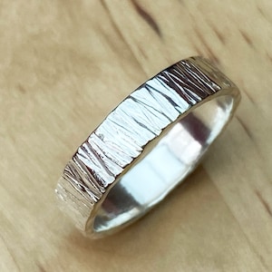 May include: A silver ring with a textured, hammered finish. The ring is smooth on the inside and has a polished look.
