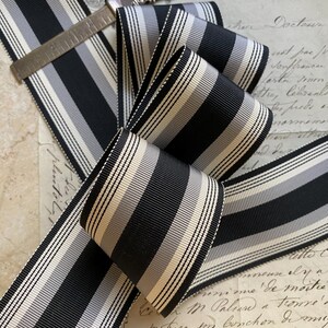 May include: Black and white striped ribbon with a satin finish. The ribbon is folded and arranged on a piece of paper with handwritten text.