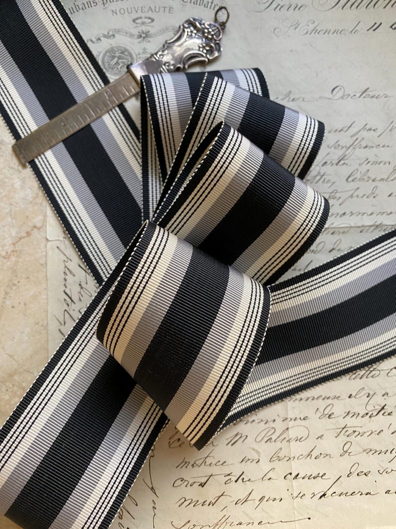 May include: Black and white striped ribbon with a satin finish. The ribbon is folded and arranged on a piece of paper with handwritten text.