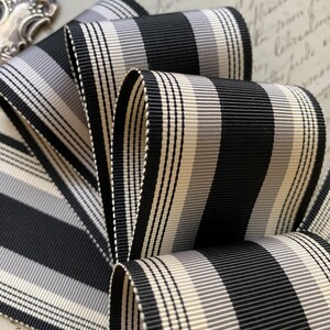 May include: Black and white striped ribbon with a cream and gray stripe. The ribbon is folded and has a textured surface.
