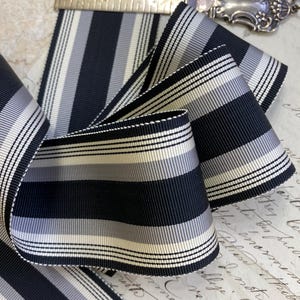 May include: Black and white striped ribbon with a subtle sheen. The ribbon has a fine, woven texture and is approximately 1 inch wide.