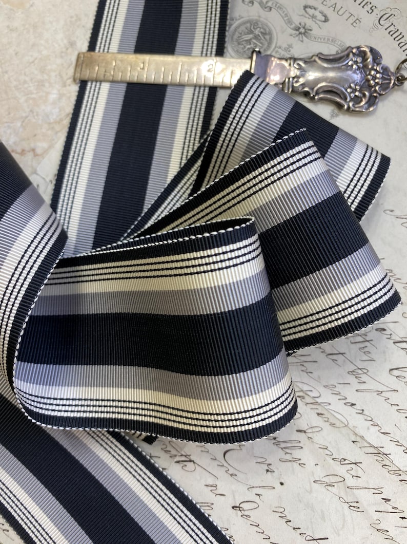May include: Black and white striped ribbon with a subtle sheen. The ribbon has a fine, woven texture and is approximately 1 inch wide.