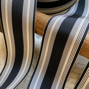 May include: Black and white striped ribbon with a subtle gray stripe. The ribbon is rolled up and displayed on a wooden surface.
