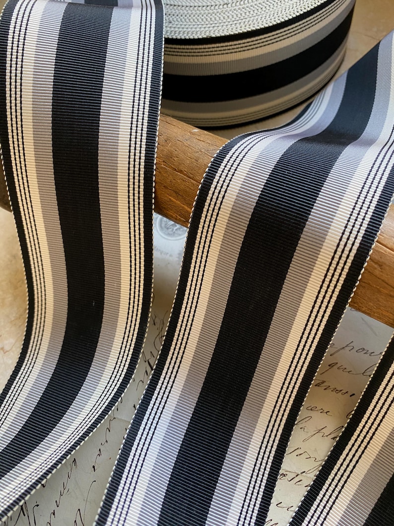 May include: Black and white striped ribbon with a subtle gray stripe. The ribbon is rolled up and displayed on a wooden surface.