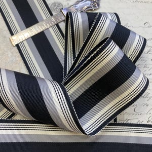 May include: Black and white striped ribbon with a subtle gray stripe. The ribbon is folded and arranged on a vintage background.