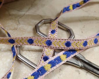 Puede incluir: Cinta rosa y dorada con diseños geométricos azules y amarillos. La cinta está envuelta alrededor de un par de tijeras plateadas.