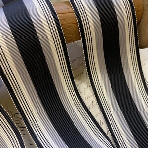 May include: Black and white striped ribbon with a subtle gray stripe. The ribbon is wound around a wooden spool.