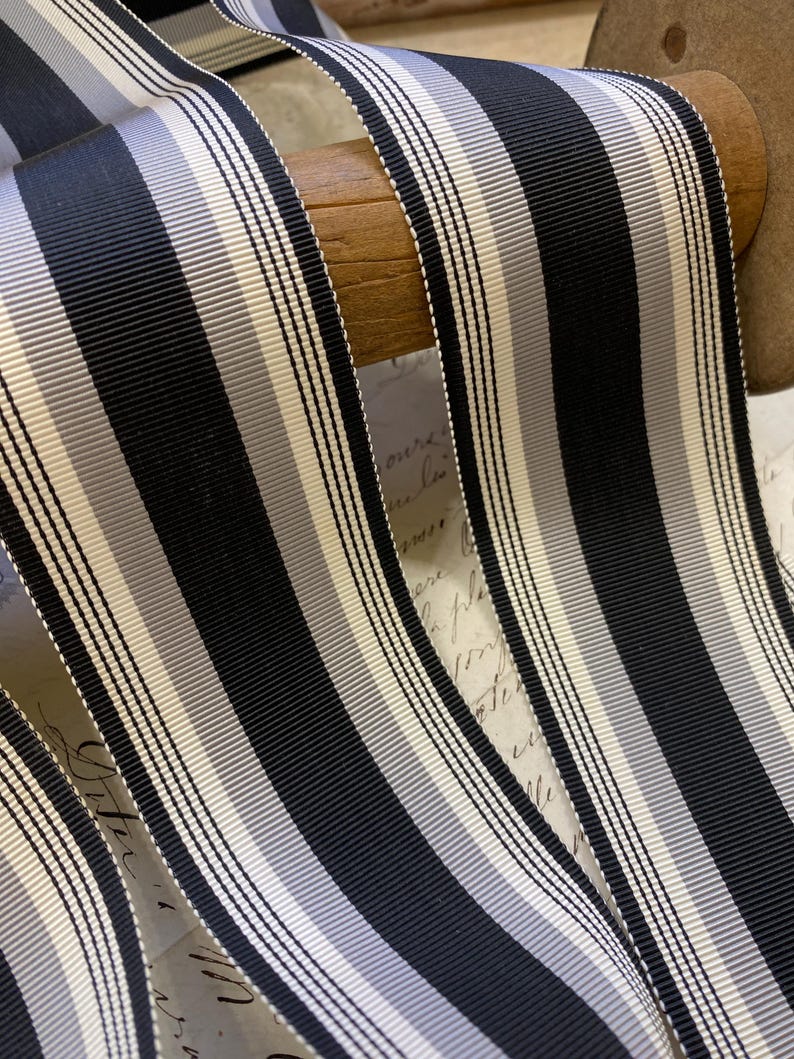 May include: Black and white striped ribbon with a subtle gray stripe. The ribbon is wound around a wooden spool.