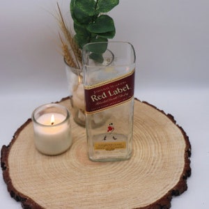May include: A clear glass vase with a red and gold label that reads "Johnnie Walker Red Label Blended Scotch Whisky". The vase is sitting on a wooden slice with a lit candle beside it.