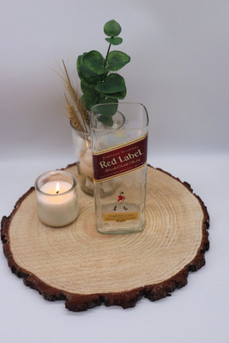 May include: A clear glass vase with a red and gold label that reads "Johnnie Walker Red Label Blended Scotch Whisky". The vase is sitting on a wooden slice with a lit candle beside it.