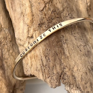May include: Gold bangle bracelet with the words "CUSTOMIZE THIS" engraved on the front.