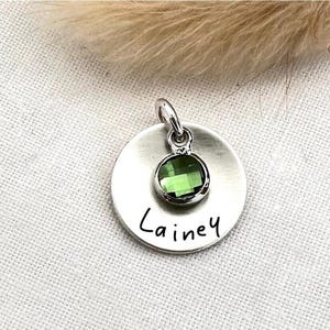 May include: Silver charm with a green gemstone and the name "Lainey" engraved on it.