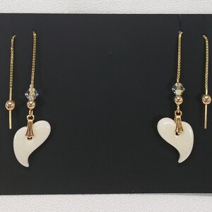 May include: A pair of gold dangle earrings with white heart-shaped charms and crystal accents.
