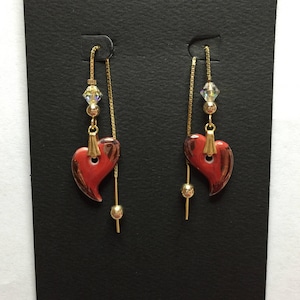 May include: A pair of dangle earrings with red heart-shaped charms and gold chains. Each charm has a gold bead and a clear crystal bead.