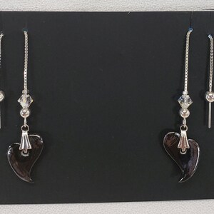 May include: A pair of dangle earrings with black heart-shaped charms and silver chains. Each earring has a small crystal bead and a silver ball bead.