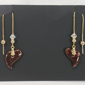 May include: A pair of dangle earrings with a brown heart-shaped charm, a gold bead, and a clear crystal on each earring.
