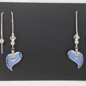 May include: A pair of dangle earrings with a silver chain and a light blue heart-shaped charm. The earrings have a small crystal bead and a silver post. The heart charm is approximately 1 inch wide.