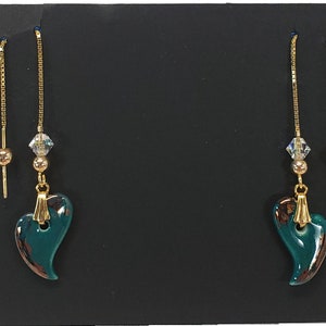 May include: A pair of gold dangle earrings with a teal heart-shaped charm and a small crystal bead. The earrings have a delicate chain that hangs from the charm.