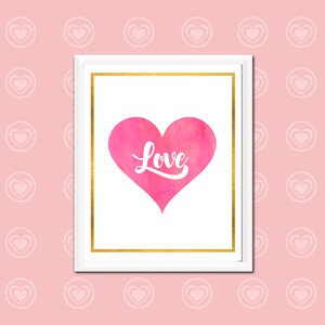 May include: A white frame with a gold border, containing a pink watercolor heart with the word "Love" written in white inside. The frame is against a pink background with a pattern of white hearts.