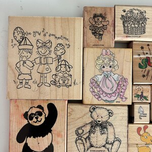 May include: A collection of wooden stamps with various designs. One stamp features three children with ice cream and the text "In the good ol' summertime." Other stamps depict a teddy bear, a panda, and a girl holding hearts.