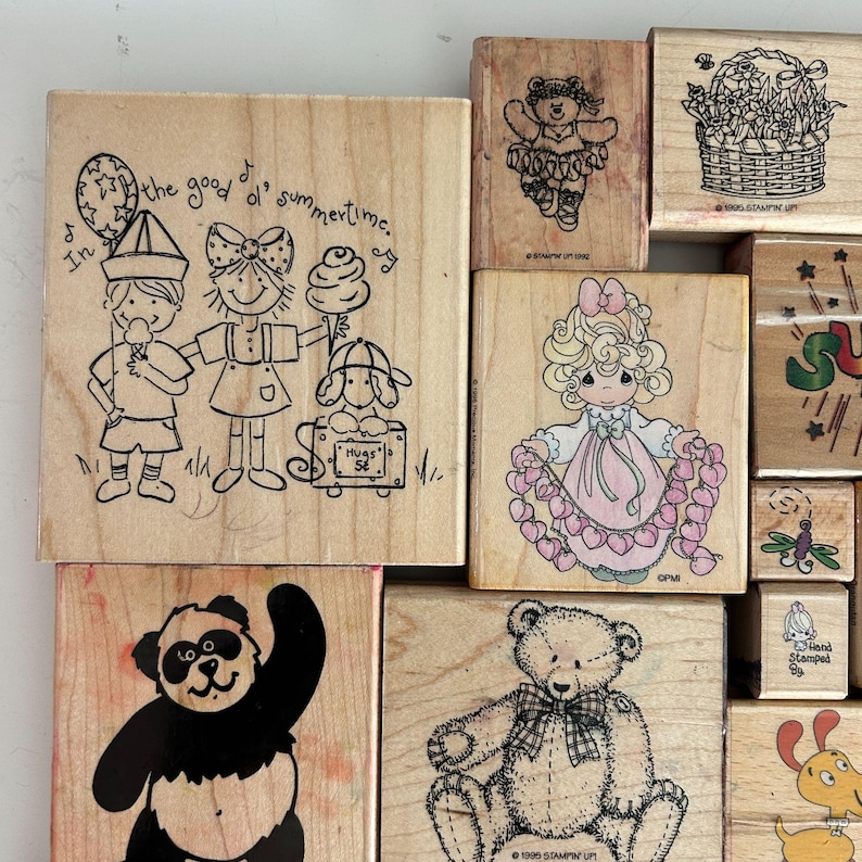 May include: A collection of wooden stamps with various designs. One stamp features three children with ice cream and the text "In the good ol' summertime." Other stamps depict a teddy bear, a panda, and a girl holding hearts.
