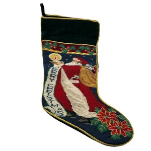 May include: Needlepoint Christmas stocking featuring Santa Claus with a sack of toys. The stocking has a dark blue background with a red and white Santa design, green holly, and the words "Merry Christmas". The top is green velvet.