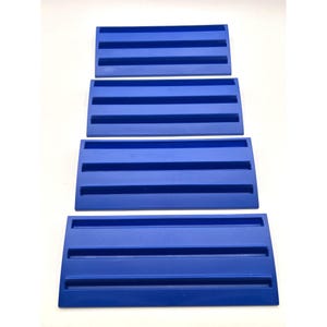 May include: Four rectangular, cobalt blue plastic trays with parallel grooves. The trays are arranged in a vertical stack against a white background. The grooves run horizontally across the width of each tray.