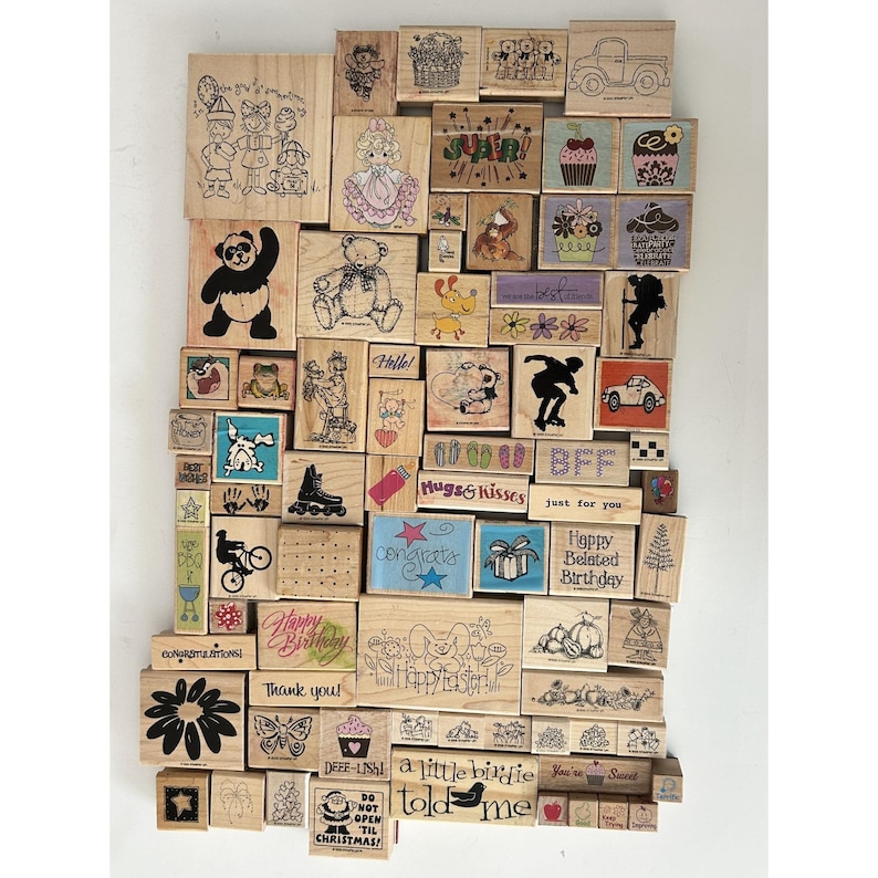 May include: A collection of various wooden rubber stamps with different designs. The stamps feature images of a panda, teddy bear, cupcakes, and text like "Hello!", "Happy Birthday", and "Congrats".