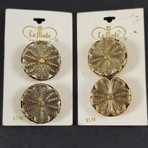 May include: Four gold-colored metal buttons with a floral design. The buttons are packaged on two cards with the text "La Mode Buttons" and "$1.98" printed on them.