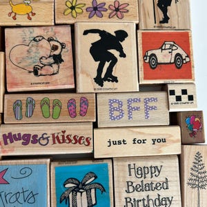 May include: A collection of wooden stamps with various designs, including flowers, a roller skater, a car, flip-flops, a teddy bear, and the words "BFF", "Hugs & Kisses", and "just for you".