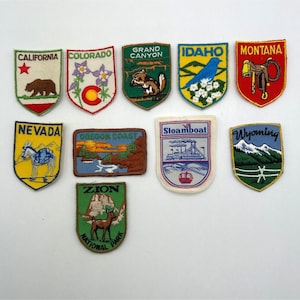 May include: A collection of ten embroidered souvenir patches featuring various US states and landmarks, including California, Colorado, Grand Canyon, Idaho, Montana, Nevada, Oregon Coast, Steamboat, Wyoming, and Zion National Park with colorful designs.