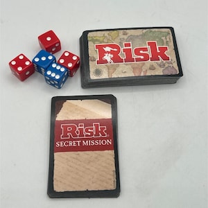 May include: A board game set with red and blue dice, and a deck of cards. The cards are labeled "Risk" and "Secret Mission". The game cards have a world map design.