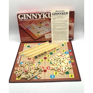 May include: A vintage Ginnykub crisscross rummy game set. The game includes a brown box with the game name, a game board, ivory-colored tiles, and instructions. The game board has numbers and spaces for the tiles.