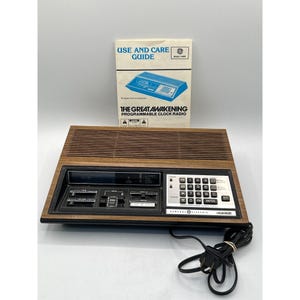 May include: A vintage General Electric The Great Awakening programmable clock radio with a wood-grain finish, black control panel, numeric keypad, and slider switches. Includes a paper Use and Care Guide manual with a blue illustration of the radio.