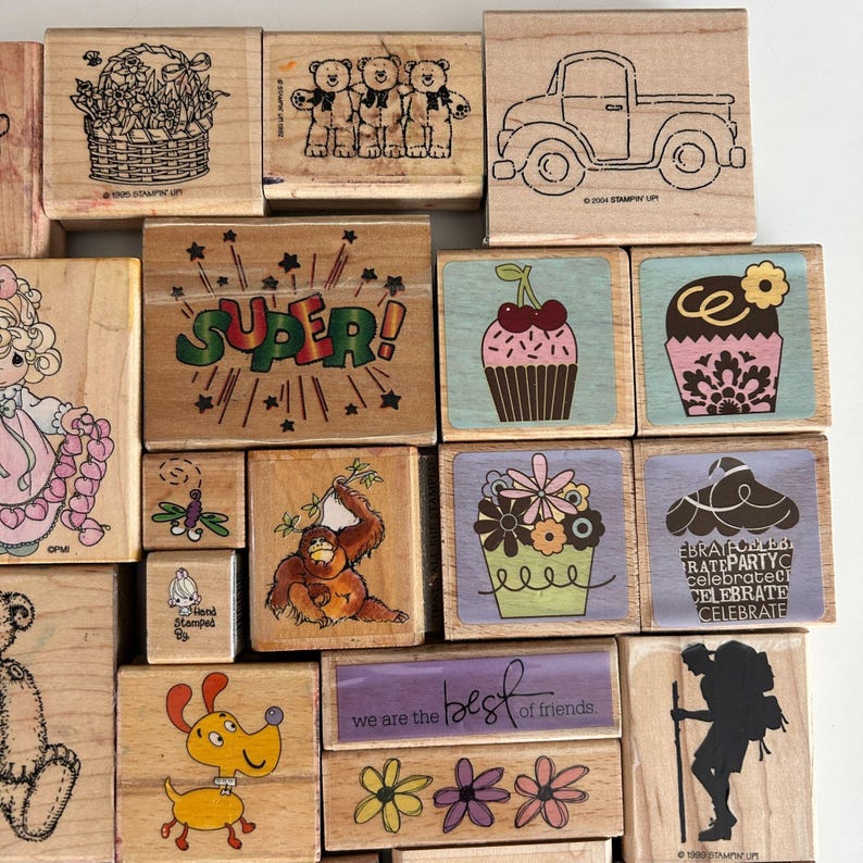 May include: A collection of wooden stamps with various designs. Images include a basket of flowers, three teddy bears, a truck, a cupcake with cherries, a cupcake with a flower, the word "SUPER!", a dragonfly, a monkey, a dog, and the text "we are the best of friends."