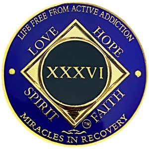 Puede incluir: Una moneda redonda dorada y azul con un diamante negro en el centro. El diamante tiene las palabras "LOVE", "HOPE", "SPIRIT" y "FAITH" en los puntos. El centro del diamante tiene el número romano "XXXVI" y las palabras "LIFE FREE FROM ACTIVE ADDICTION" y "MIRACLES IN RECOVERY" están alrededor del borde.