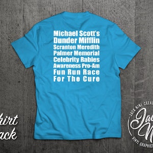 May include: A turquoise blue t-shirt with white text on the back that reads "Michael Scott's Dunder Mifflin Scranton Meredith Palmer Memorial Celebrity Rabies Awareness Pro-Am Fun Run Race For The Cure". The bottom of the shirt has a white logo that reads "Jack Nine Creative Vinyl Graphics Design Apparel".