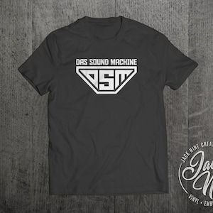 May include: A black t-shirt with a white graphic of a triangle with the letters "DSM" inside and the text "DAS SOUND MACHINE" above it. The text "Jack Nine Creative" is printed in a circle on the bottom right of the shirt.