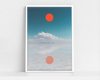May include: A framed photograph of a minimalist landscape with a single red circle in the sky and a reflection of the circle in the water below. The sky is blue and there are white clouds in the background.