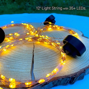 May include: A 12-foot light string with 35+ LEDs. The string features warm yellow lights on a copper wire, with black caps. The lights are arranged on a wooden surface.