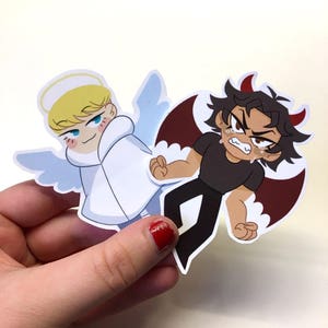 May include: Two cartoon character stickers, one an angel with a halo and white wings, the other a devil with red wings and horns. The angel is smiling and the devil is crying.