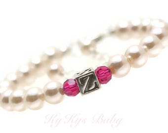 May include: A white pearl bracelet with a silver charm featuring the letter "Z" and two pink crystal beads.