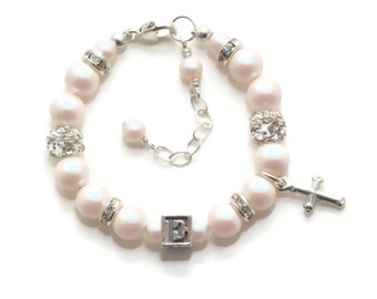 May include: A white pearl bracelet with a silver charm, a silver cross charm, and a silver charm with the letter 'E'.