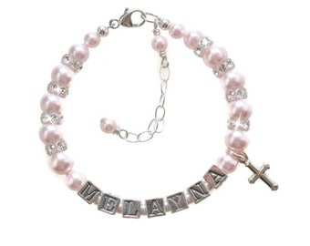 May include: A pink pearl bracelet with a silver cross charm and a name spelled out in silver letter beads. The name is "MELAYNA".