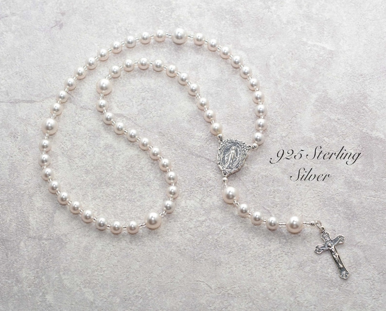 White pearl prayer beads on gray background. Pearls are spaced by silver lined clear seed beads. It has a sterling silver Virgin Mary Rosary Center charm and Sterling Silver Crucifix pendant.