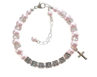 May include: A pink pearl bracelet with a silver cross charm and a name spelled out in silver letter beads. The name is "MELAYNA".