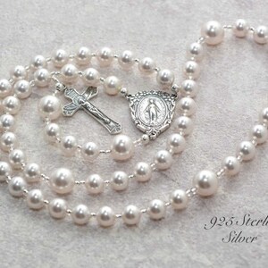 White pearl prayer beads on gray background. Pearls are spaced by silver lined clear seed beads. It has a sterling silver Virgin Mary Rosary Center charm and Sterling Silver Crucifix pendant.